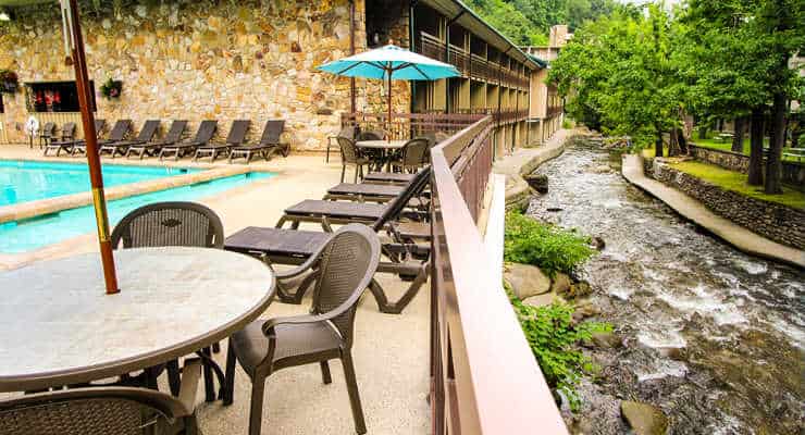 Lounge chairs and tables with umbrellas between a creek and a swimming pool.