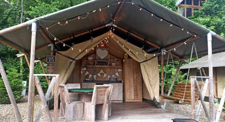 Open outdoor canvas tent with rustic swing, table and chairs, and hanging lights.