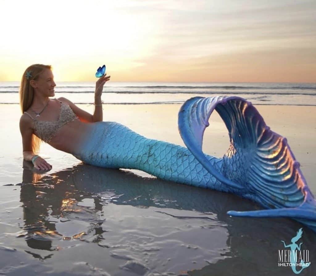 Mermaid lying on the beach with a butterfly on her hand