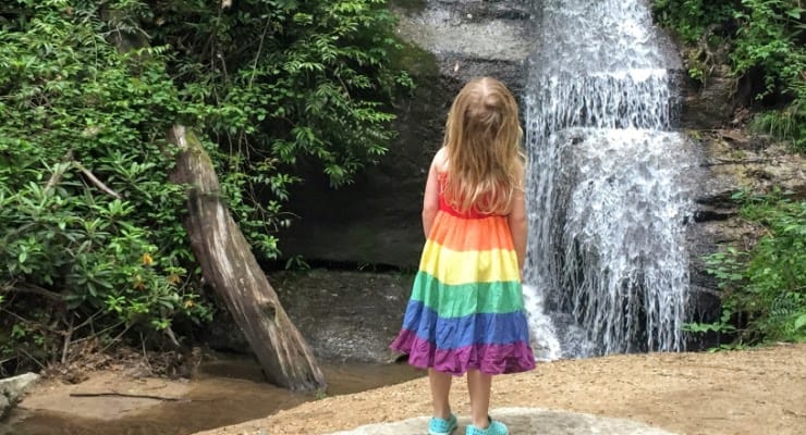 Girl in rainbow dress looking up at a waterfall