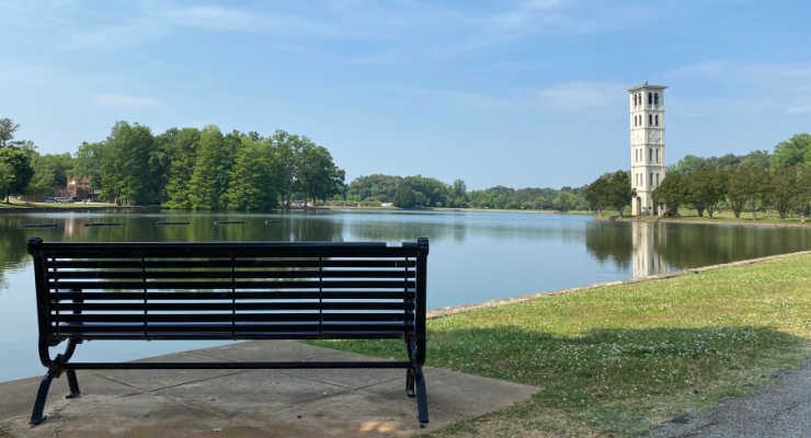 Black bench across the lake from Furman with the clock tower.
