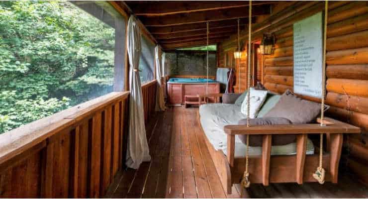 A large porch swing and a hot tub on a covered porch of a wooden cabin. Photo Credit: AirBnb