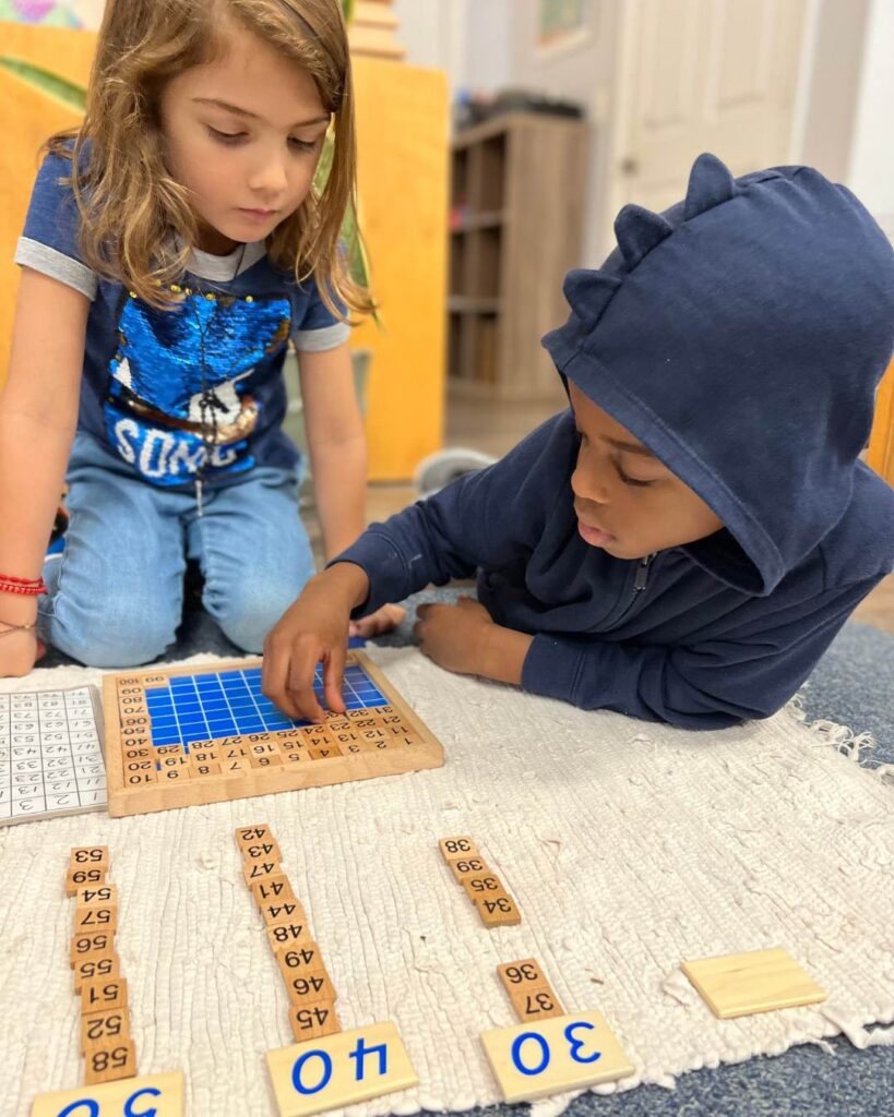 Two children work together on a math board, arranging number tiles and checking their work during a shared learning activity.