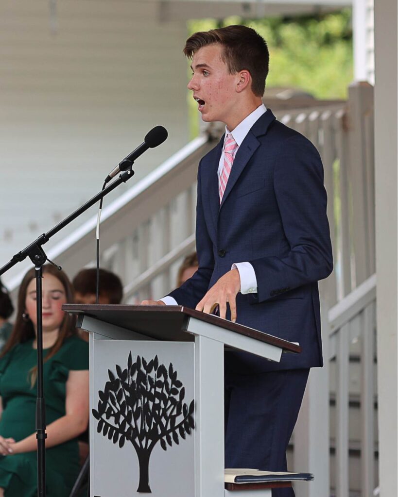 A student speaks confidently at a podium during a school event, practicing public speaking and leadership skills.