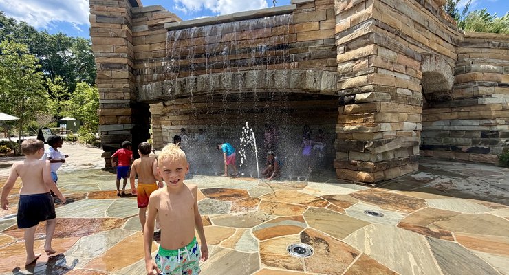 Child smiling at the Watermill Mountain waterfall and splash pad at Gipson Play Plaza Dorothea Dix Park Raleigh NC