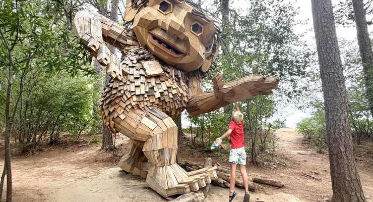 Giant Thomas Dambo recycled wood troll sculpture in the pine forest at Dorothea Dix Park Raleigh NC with child standing nearby