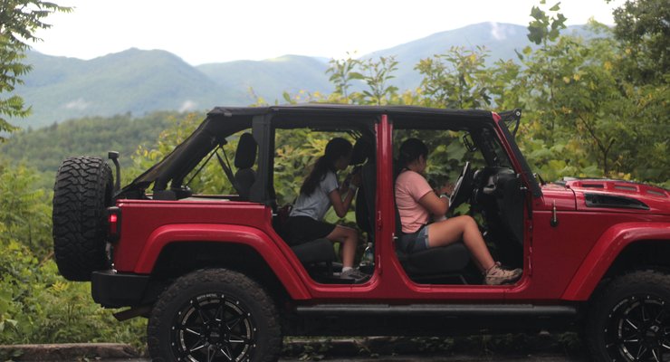 Family sitting in a red Jeep Wrangler with doors off and Smoky Mountain views in the background near Gatlinburg, TN