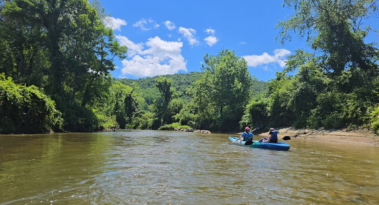 Family kayaking on the clear French Broad River at Headwaters Outfitters in Rosman NC with mountain views