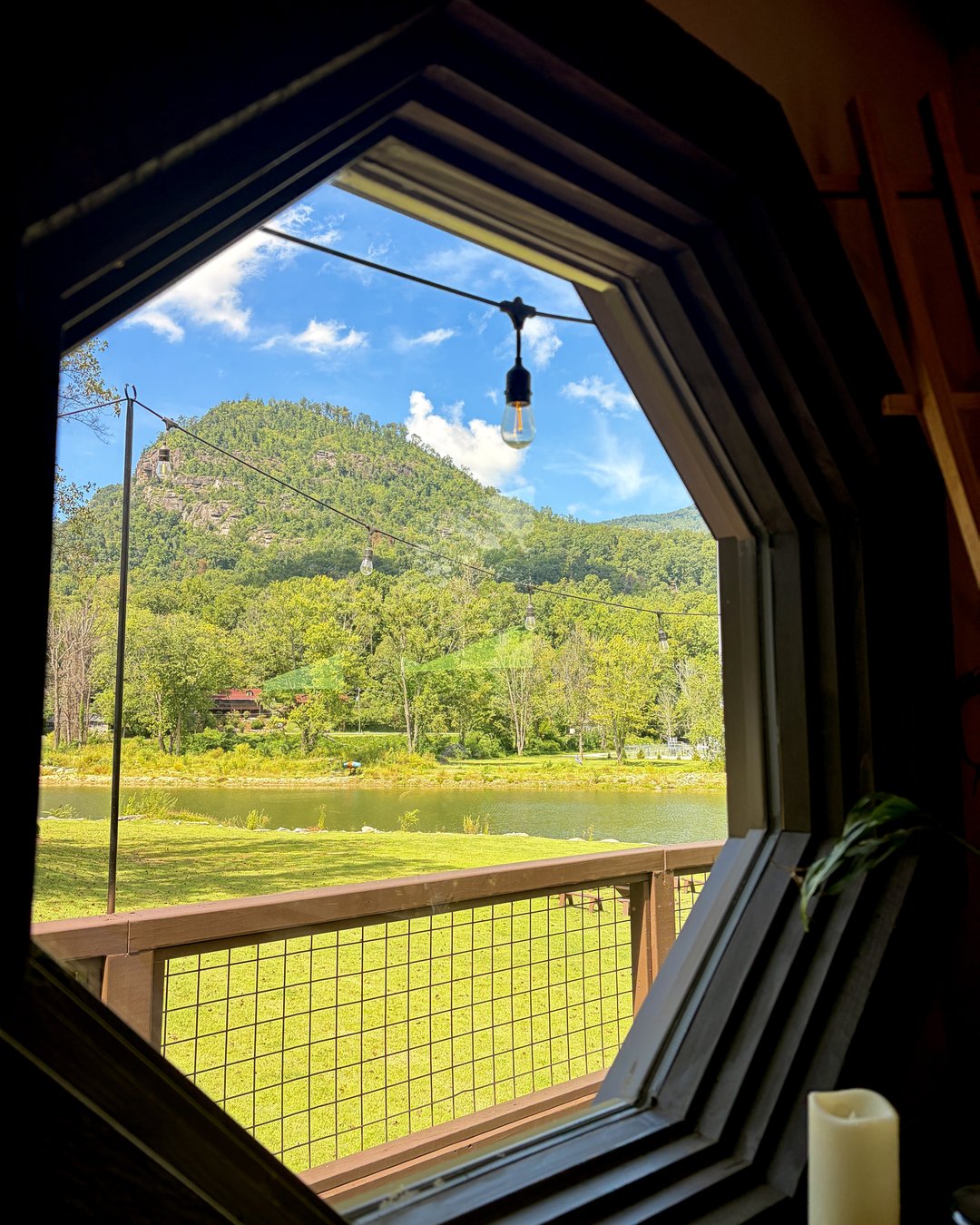 View through a large octagonal window at Fae Nectar looking out over the green lawn river and Blue Ridge Mountains