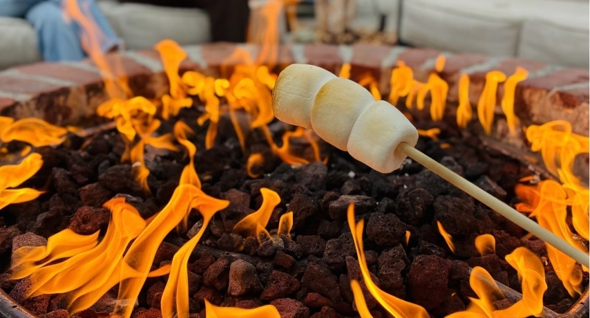 Three marshmellows on a skewer roasting over a fire pit
