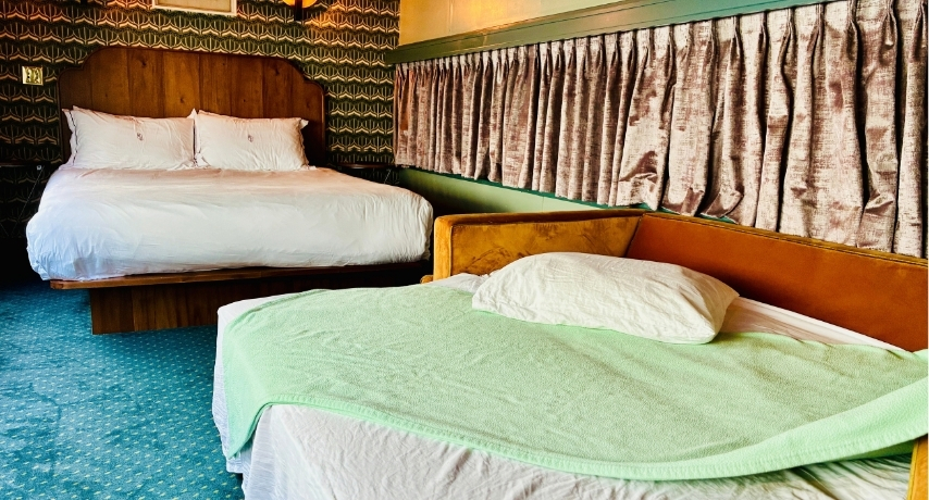 A trundle bed made up with pillow and blanket in front of a queen-sized bed inside a train carriage
