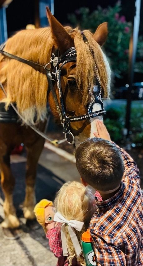 A boy and a girl stroke the nose of a tall horse
