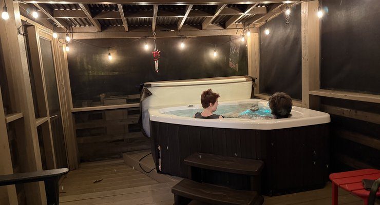 Two teens soaking in a covered hot tub on a screened porch under string lights at a Bryson City cabin